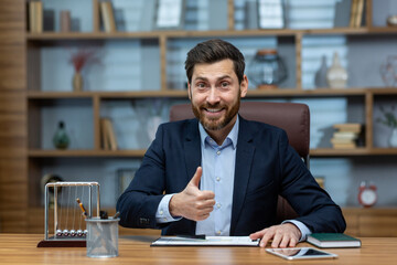 Smiling mature businessman in suit approves with thumbs up, showcasing productivity in a tidy home...