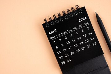 April 2024 Black spiral desktop calendar and wooden pencil.