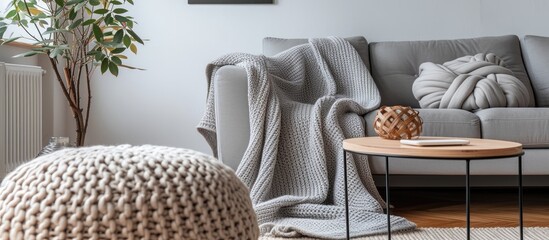 Soft blanket draped over a cozy grey sofa, coffee table, and pouf in living room.