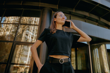 Young woman manager is talking mobile phone whiile standing on modern building background
