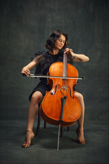 Cellist, elegant woman in deep concentration, playing cello passionately with eyes closed against vintage green background. Concept of classical art, retro style, music, inspiration © master1305