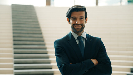 Smart caucasian business man standing with folded arm while looking at camera. Professional handsome project manager pose at camera while smiling with confident with blurred background. Exultant. - Powered by Adobe