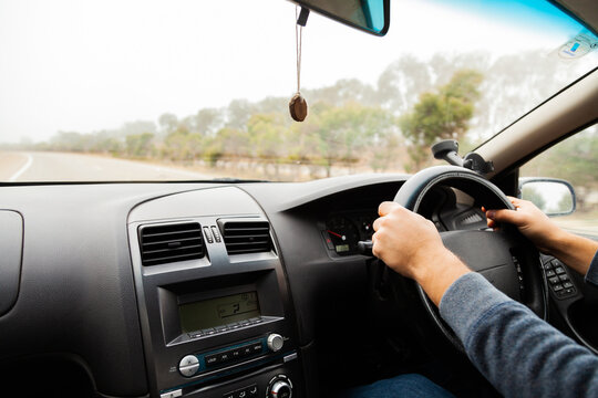 Man's hands on car steering wheel driving in foggy conditions