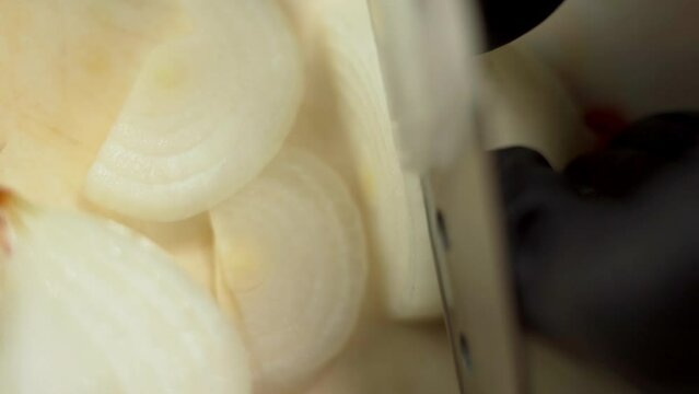 Chef in black gloves slicing onion into thin slices for preparing a burger.