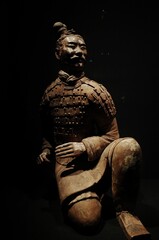 Sculpture of an Asian warrior, standing with his hands on his hips, illuminated in the darkness