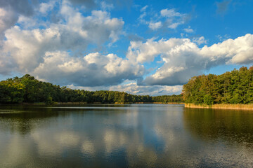 Obraz premium Natural landscape of the lake, high definition, the movement of waves against the background of the autumn forest. The reflection of clouds on the ripples of water. Germany.