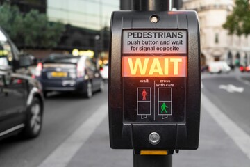 Closeup of a pedestrian button on the road with wait writing, traffic blurred background