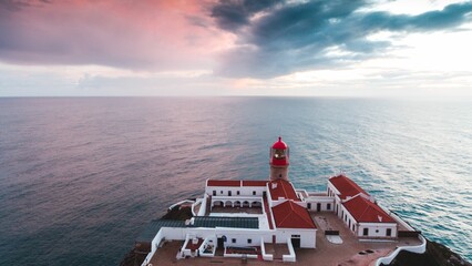 View of a red lighthouse with a house on the shoreline in Portugal, Algarve at sunset