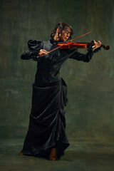 Dynamic pose of passionate female musician, young woman, violinist in black attire, playing violin...