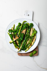 Grilled green spring vegetables: zucchini, asparagus, broccolini on white marble background. Top view, copy space. .