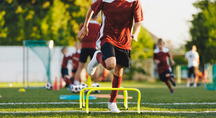 Fototapeta premium Teenagers on physical education training with a coach. Sporty kids exercising and jumping over hurdles on the training field. Sport school training for elementary age class.