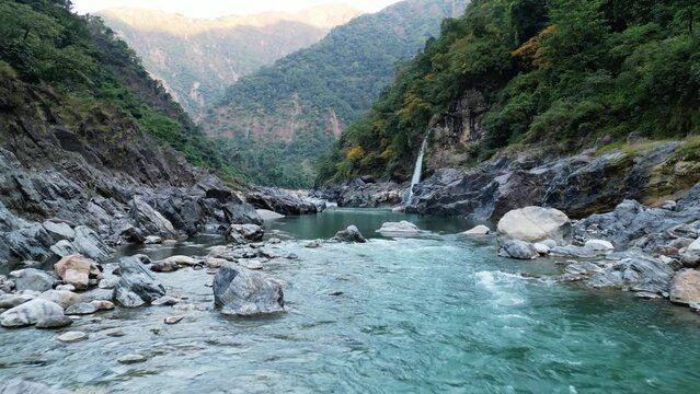 Crystal clear river with a waterfall between rocky mountains covered with trees