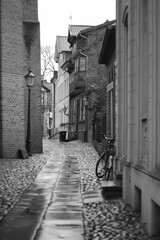 Greyscale vertical shot of a narrow alleyway between two brick buildings