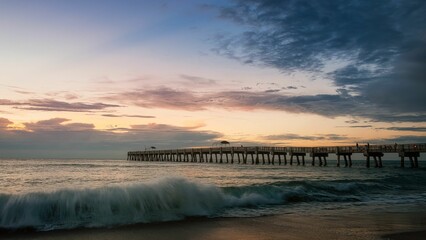 a pier with waves crashing over the shore during the sunset