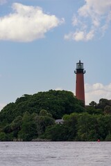 Lighthouse situated on a rocky coast surrounded by lush, green trees in Jupiter, Florida. © Wirestock