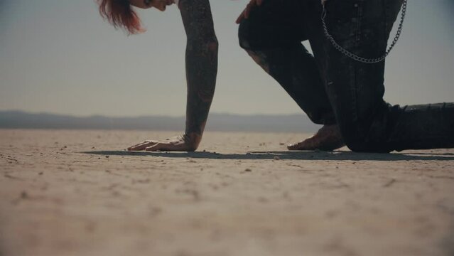 Never give up. Exhausted barefoot man walking through desert in pain and falls on his knee. Guy gets up and keep walking. Cinematic shot in slow motion. Dry lake. Warm color correction, 4k
