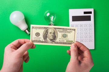Male hand hold money, dollar flatlay led bulb, incadenscent lamp and edison on green background. Economy and ecology save.