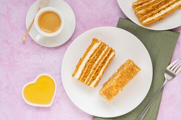 Dessert, sliced layered honey cake with cream on a white plate on a pink concrete background. Valentine's day concept.