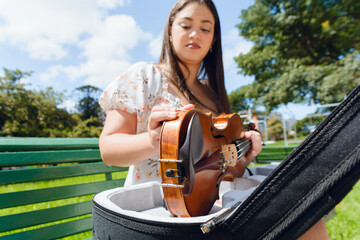 blurred young latin woman, sitting outdoors taking her violin out of case, focus on musical...