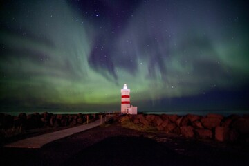 Majestic lighthouse situated on a rocky shore illuminated with a bright green light