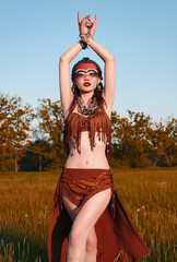Outdoor portrait of pretty young shamaness (witch doctor). Beautiful shaman (sorceress) dancing in...