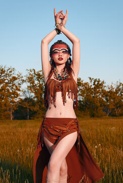 Outdoor portrait of pretty young shamaness (witch doctor). Beautiful shaman (sorceress) dancing in field at sunset