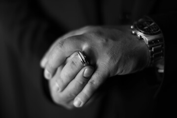 Greyscale close-up of an man's hands as he places his wedding ring on his finger
