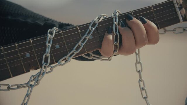 Close up with gothic women playing on scratched guitar with chains in slow motion. Dark nails. Pitch Black. Warm color correction, 4k