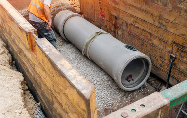 Builder installing big diameter concrete drainage pipe protected by trench support system during deep drainage works