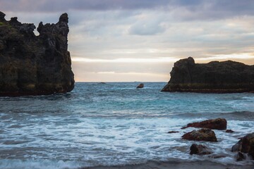 a beach with a rock formation near the ocean and some waves