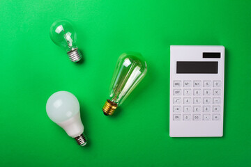 The concept of savings electricity. Reducing the payment of utility bills. A incandescent lamp, edison, calculator and led bulb on a green background. Flat lay, top view.