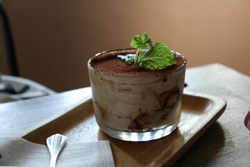 Delicious tiramisu dessert in the glass presented on a rustic wooden tray, situated on a table