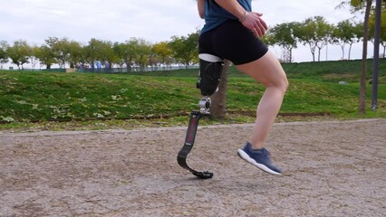 Unrecognizable male runner with prosthetic sports leg on park path. Incognito athletic amputee enjoys running, embodying adaptive sports spirit. - Powered by Adobe