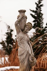 A statue is outside in the snow and is near plants.