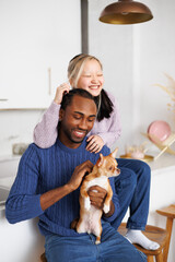 Smiling young asian woman hugging african american boyfriend with dog in kitchen