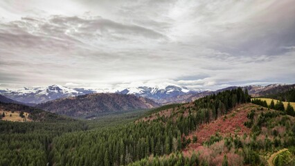 the view over a valley on a cloudy day with snow capped mountains