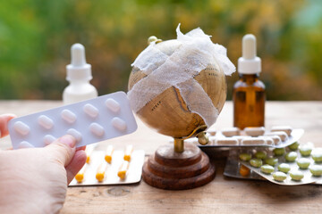 doctor's hand holding out blister pills, bandaged globe, planet sick concept, medicines and pills,...
