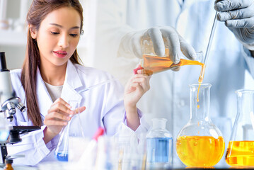 Attractive scientist woman looking chemical sample in flask at laboratory with lab glassware background. Science or chemistry research and development concept.	
