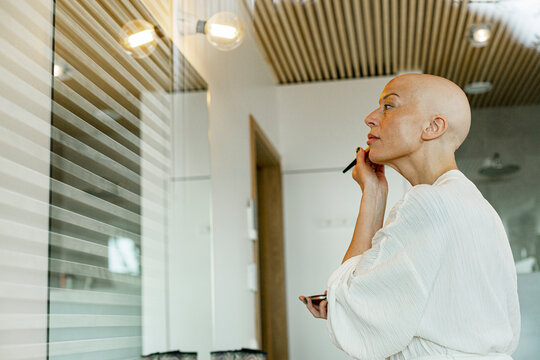 Woman suffering from cancer applying blusher on cheek at home