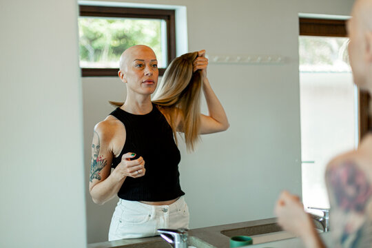 Reflection of woman with cancer removing wig while standing in bathroom