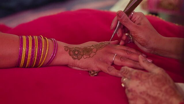 Close-up shot of a woman's hands drawing on another hand with henna paste