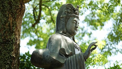 Fototapeta na wymiar Aged Hindu goddess Devi statue stands on a lush green backdrop of trees