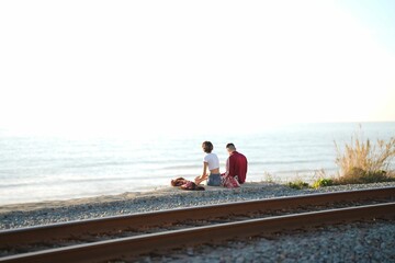 People seated side-by-side on a railroad track overlooking an ocean