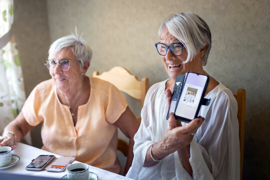 Happy senior women showing picture on smart phone by female friend at home