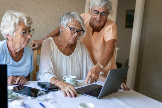 Elderly female friends using laptop on dining table at home