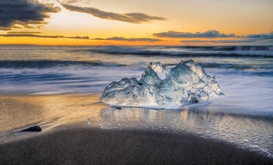 Piece of the iceberg on the beach against a scenic sunset