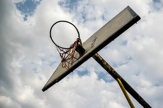 Low angle shot of a rusty old basketball hoop under a cloudy blue sky - Powered by Adobe
