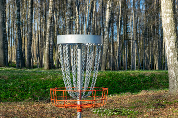 a disc golf hole on green grass with birch grove in background, disc golf basket in a park