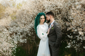 a bearded groom plays and a girl with green hair against the background of blooming spring