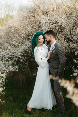 Fototapeta na wymiar a bearded groom plays and a girl with green hair against the background of blooming spring
